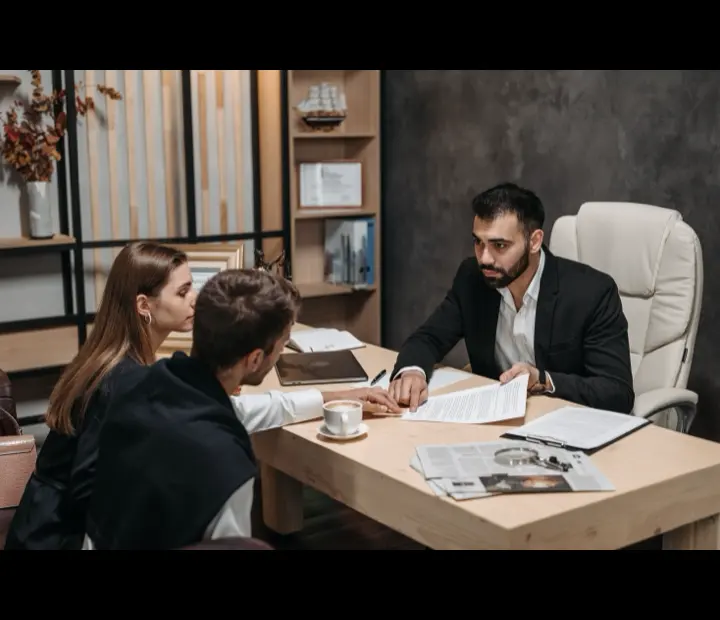 A couple reviewing paperwork with their accountant across a table.