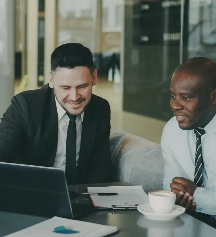 Two people talking over a laptop in a bright office.