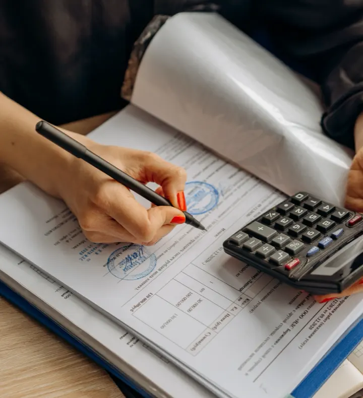 An accountant signing paperwork beside a calculator and folders.
