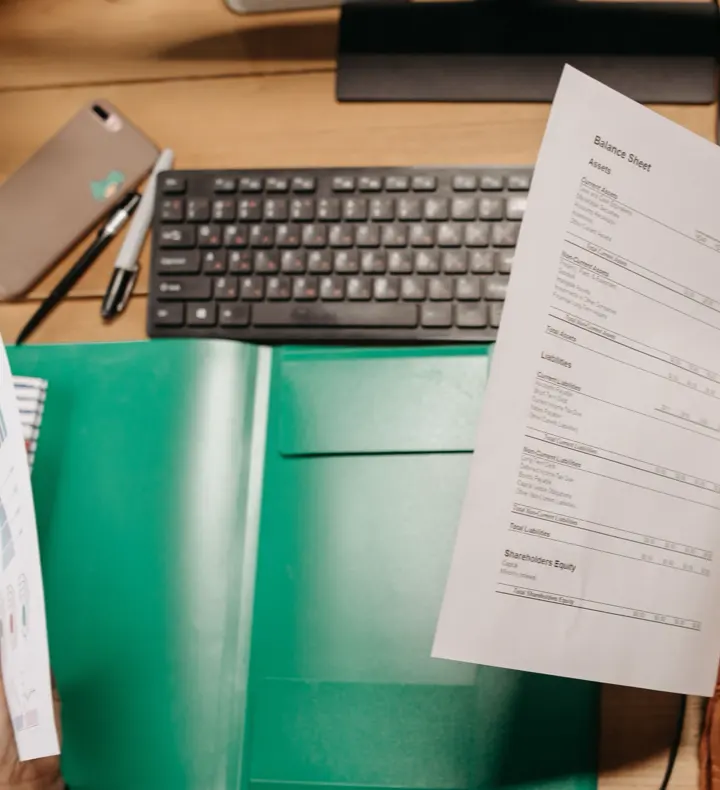 Hands reviewing a printed balance sheet over a desk and keyboard.