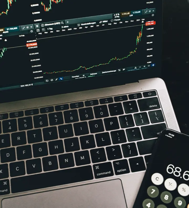 A laptop showing trading charts beside a calculator and phone.