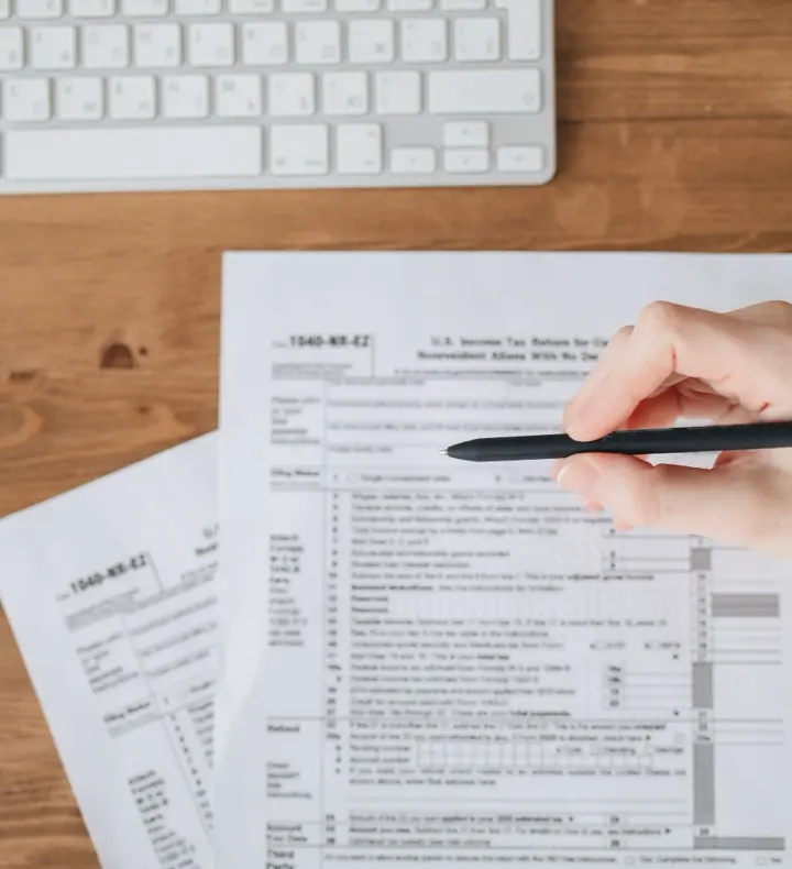 A hand holding a pen over a US tax form on a wooden desk.