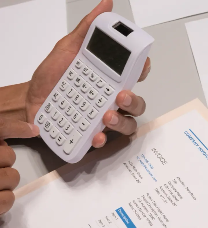 Close-up of hands using a calculator next to a printed invoice.